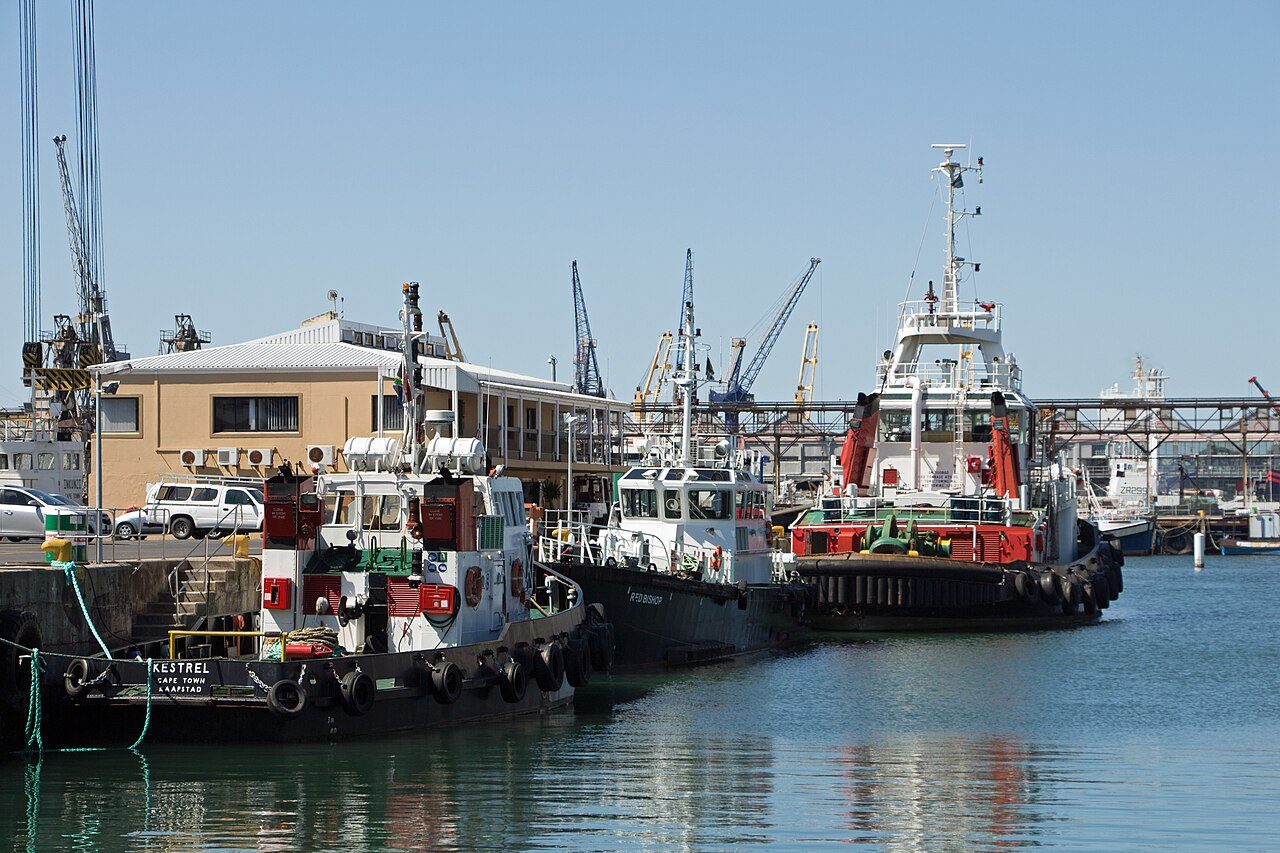 Harbour tugboats and a pilot boat moored alongside a quay in the Port of Cape Town, with dockside cranes behind